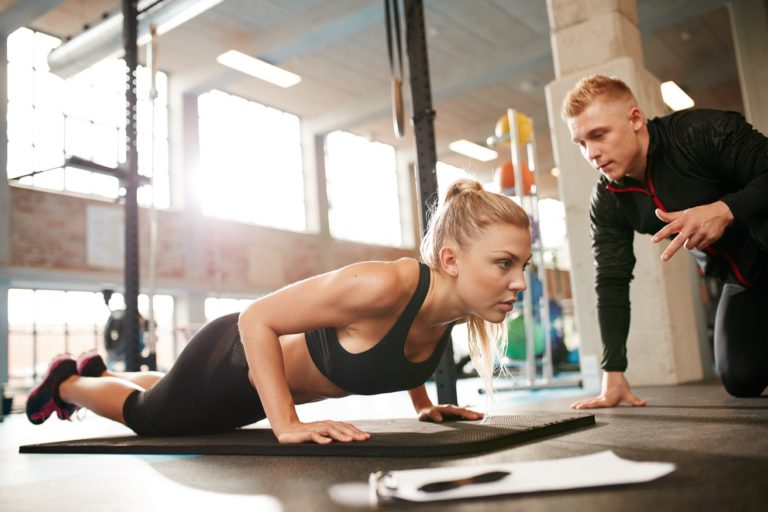 Indoor shot of young female exercising with personal trainer at gym. Fitness woman doing push ups with her personal trainer at health club.