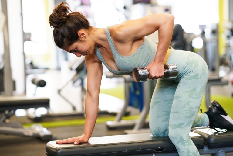 Caucasian strong woman lifting some weights and working on her triceps and biceps in a gym with dumbbells.