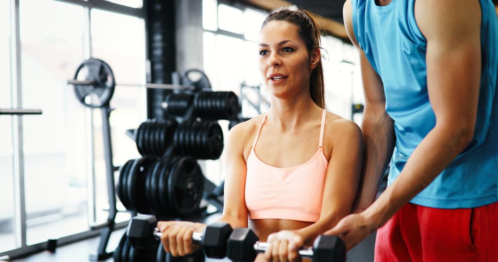 Personal trainer helping beautiful woman in gym