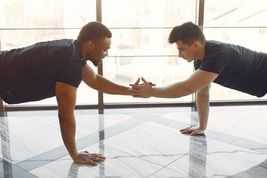 Sports men in the gym. A black man performs exercises. Guy in a black t-shirt. Internationals friends.