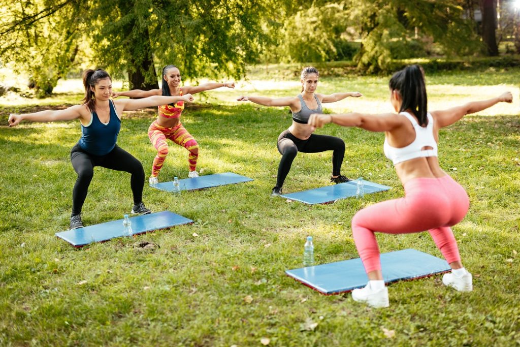 Beautiful girlfriends doing squats exercise in the park with female fitness trainer.